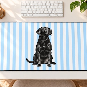 Puede incluir: Una alfombrilla de escritorio rectangular con un patrón repetitivo de rayas verticales en azul claro y blanco. Centrada en la alfombrilla hay una ilustración detallada de un labrador retriever negro sentado mirando hacia arriba con atención.