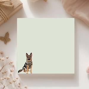 May include: A light green square notepad featuring a watercolor illustration of a German Shepherd dog. The dog is depicted in a sitting position with black, brown, and tan fur. The notepad is surrounded by decorative elements.