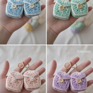 Op de afbeelding: Vier paar gehaakte rugzak sleutelhangers in pastelkleuren: blauw, groen, roze en paars. Elke sleutelhanger heeft een knoopsluiting en een goudkleurige ring. De sleutelhangers zijn handgemaakt.