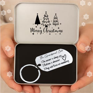 May include: A silver keychain with a ring, presented in a silver tin. The keychain features the text "The Grandparent Code" and three rules. The tin lid has a Christmas tree design and the words "Merry Christmas".