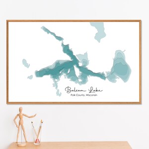 Puede incluir: Una impresión enmarcada que presenta un mapa detallado del lago Balsam en el condado de Polk, Wisconsin. El lago se representa en tonos de azul y turquesa sobre un fondo blanco. La impresión está dentro de un marco de madera marrón claro, con el nombre del lago escrito.