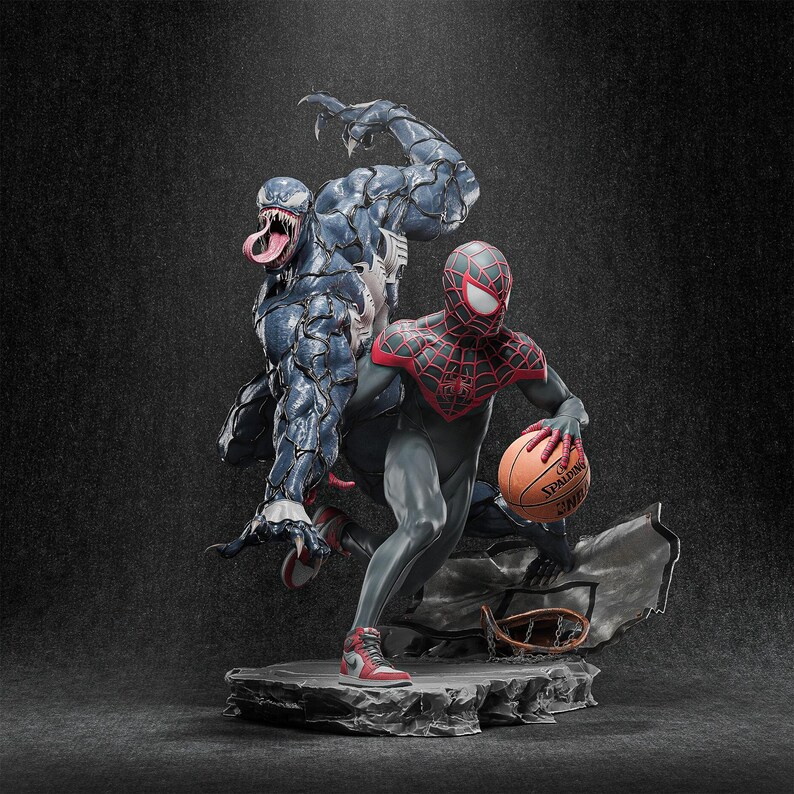 May include: A detailed statue featuring Spider-Man, in a black and red suit, dribbling a basketball. Behind him is a large, blue Venom figure. The statue is set on a rocky base with a basketball hoop.