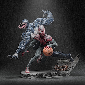 May include: A detailed statue featuring Spider-Man in a black and red suit, holding a Spalding NBA basketball, with Venom looming behind. The figures are on a rocky base, with a dark background.