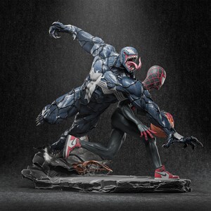 May include: A dynamic statue featuring Venom and Spider-Man in action. Venom, in dark blue with white accents, lunges towards Spider-Man, who wears a red and black suit and red trainers. The base is a textured grey stone.