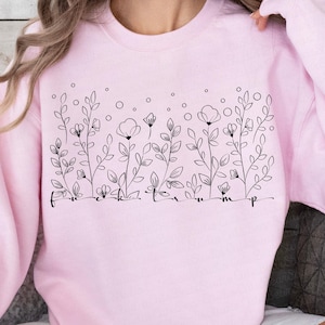 Może przedstawiać: Jasnoróżowa bluza z czarnym kwiatowym wzorem i napisem "f**k trump". Wzór zawiera stylizowane kwiaty, liście i kółka. Bluza jest w jednolitym, jasnoróżowym kolorze.