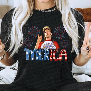 May include: Black t-shirt featuring a red, white and blue American flag design. The flag has the word "MERICA" written on it. A man with a bandana and a backwards baseball cap is in the centre of the flag. He is wearing a red, white and blue shirt with the words "Rock Roll" on it. There are fireworks around the flag.