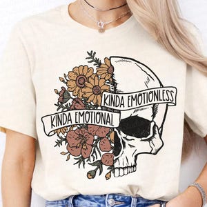 May include: A white t-shirt with a graphic of a skull with flowers on one side and the text "Kinda Emotional" and "Kinda Emotionless" on the other.