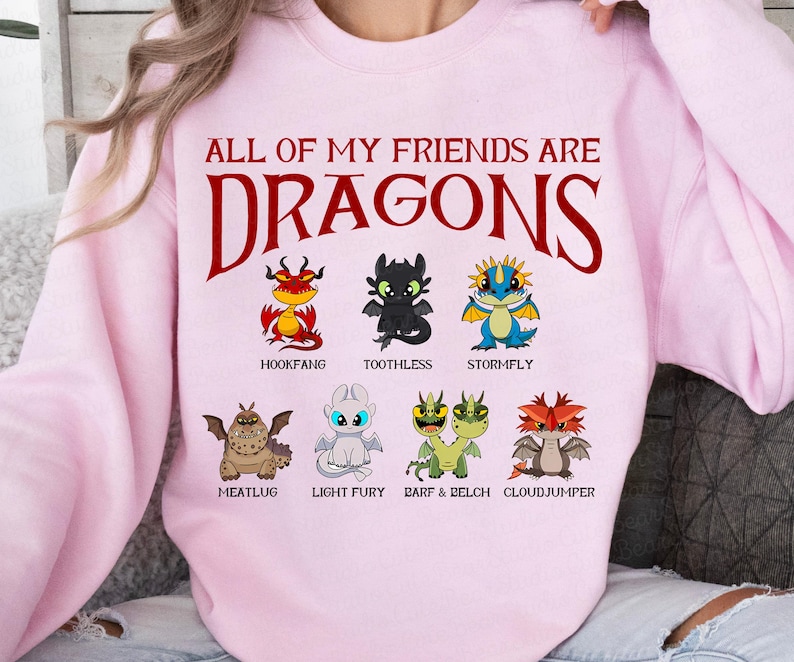 K&ouml;nnte beinhalten: Hellrosa Sweatshirt mit dem roten Schriftzug "ALL OF MY FRIENDS ARE DRAGONS". Darunter befinden sich Cartoon-Drachen, darunter Hookfang und Toothless. Das Sweatshirt hat einen Rundhalsausschnitt.