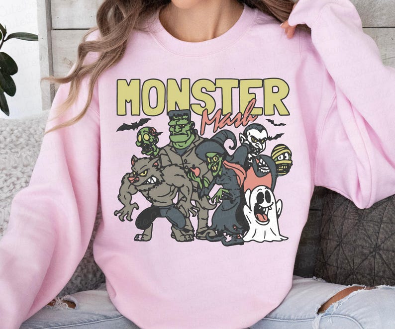 May include: A pale pink sweatshirt with a cartoon illustration of classic monsters such as a werewolf, Frankenstein's monster, a witch, and a vampire. The words "MONSTER Mash" are printed above the characters in yellow and black.