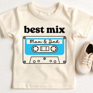Könnte beinhalten: Ein weißes T-Shirt mit einem schwarzen und blauen Kassettenband-Motiv. Der Text "best mix" befindet sich über dem Band und der Text "Mom & Dad" auf dem Band.
