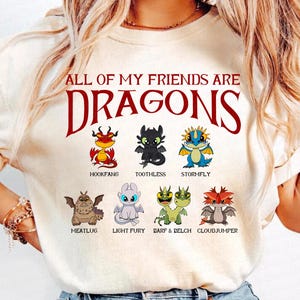 K&ouml;nnte beinhalten: Cremefarbenes T-Shirt mit dem Text "ALL OF MY FRIENDS ARE DRAGONS" in Burgunderrot. Darunter sind Cartoon-Drachen, jeder mit einem einzigartigen Design und Namen: Hookfang, Toothless, Stormfly, Meatlug, Light Fury, Barf & Belch und Cloudjumper.