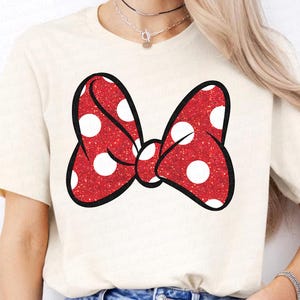 May include: A white t-shirt with a red and white polka dot bow printed on the front.