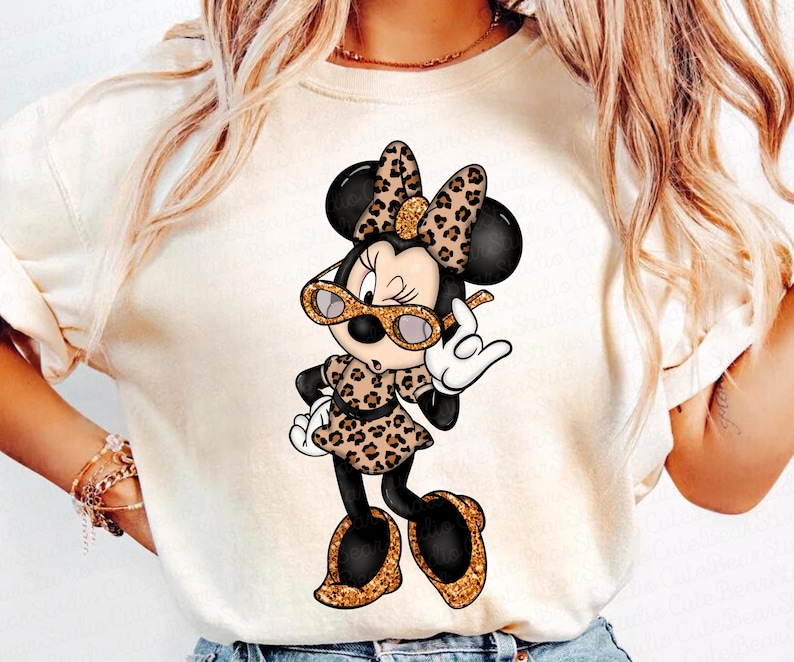Może przedstawiać: Biały t-shirt z kresk&oacute;wkowym obrazkiem Minnie Mouse w okularach przeciwsłonecznych w panterkę i sukience w panterkę. Podnosi rękę w geście pokoju.