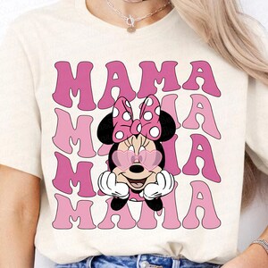 May include: A white t-shirt with a pink graphic of Mickey Mouse wearing heart-shaped sunglasses and the text "MAMA" repeated four times.