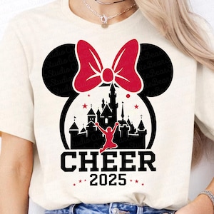 May include: A white t-shirt with a black and red design. The design features a silhouette of Cinderella's castle with a red bow and a cheerleader in the air. The text "CHEER 2025" is below the design.