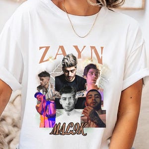 Può includere: T-shirt bianco con un collage di immagini di Zayn Malik e la scritta "ZAYN MALIK" in stile vintage. La maglietta ha maniche corte e girocollo. Un adesivo rosso e bianco "FAST DELIVERY" si trova nell'angolo in alto a sinistra.