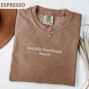 Könnte beinhalten: Ein Set aus drei Keramikbechern mit gesprenkelter, matter Oberfläche. Die Becher sind in Creme-, Hellgrau- und Dunkelgrautönen gehalten. Jeder Becher hat ein schlichtes, minimalistisches Design und einen abgerundeten Griff.