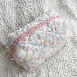 Quilted cosmetic bag with pastel floral print, pink zip, diamond-stitched texture, and rectangular shape on a white surface.