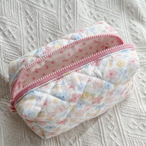 Quilted cosmetic bag with pastel floral print, pink zip, pink polka dot lining, and diamond-stitched texture.