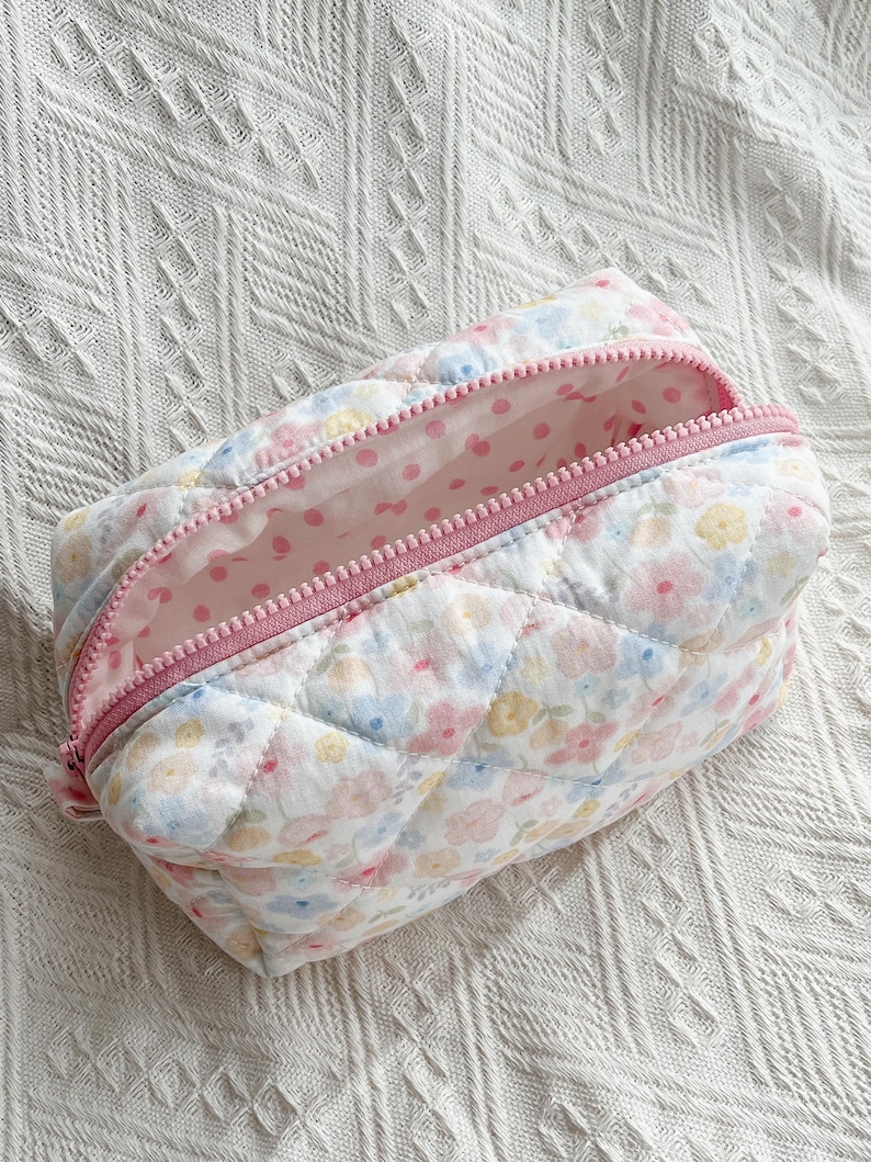Quilted cosmetic bag with pastel floral print, pink zip, pink polka dot lining, and diamond-stitched texture.