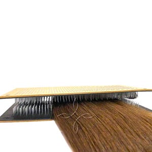 May include: A brown hair weft is being held in place by a hair wefting tool with rows of pins. The tool is made of wood and has a black base.