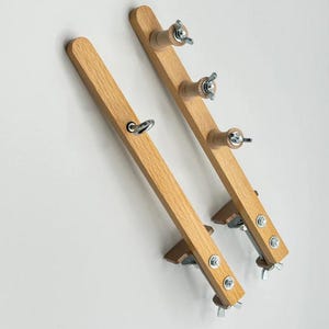 Könnte beinhalten: Zwei Holzstäbe mit Klemmen und verstellbaren Knöpfen. Jeder Stab hat drei Knöpfe zum Aufwickeln von Garn. Die Stäbe sind an Klemmen befestigt, die an einem Tisch oder einer anderen Oberfläche befestigt werden können.