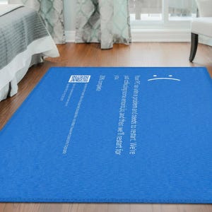 May include: A rectangular blue rug with white text and a sad face graphic. The rug has a computer error message printed on it, including a QR code and the words "20% complete."