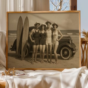 Könnte beinhalten: Sepiafarbener gerahmter Druck mit vier Personen in Vintage-Bademode und Hüten, die an einem Strand neben einem klassischen Auto und Surfbrettern stehen. Das Bild erinnert an eine nostalgische Retro-Strandszene.