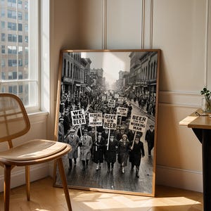 Może przedstawiać: Oprawiona czarno-biała fotografia przedstawiająca historyczny protest uliczny. Tłum niesie transparenty z napisami WE WANT BEER, REPEAL THE 18TH AMENDMENT, GIVE US BEER, DOWN WITH DRY LAWS oraz BEER FOR THE WORKING MAN na miejskiej ulicy.