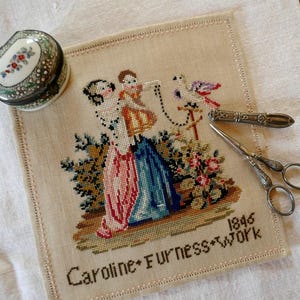 May include: A beige linen sampler featuring a cross-stitch design of two figures, a bird, and floral elements. The text reads Caroline Furness Work 1846. Included are a round floral trinket box, a silver metal needle case, and silver scissors.