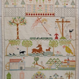 Peut inclure: Un ouvrage de broderie au point de croix sur tissu écru, représentant des motifs religieux, un agneau blanc avec un drapeau, un cerf, un perroquet, des bâtiments, des personnages, ainsi qu'un alphabet et des chiffres brodés en bas.
