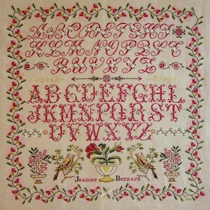 Peut inclure: Une broderie au point de croix avec un alphabet rouge et une bordure florale. Le motif comprend des lettres cursives, des chiffres et un alphabet minuscule. La broderie porte également le nom de "Jeanne Bernard".