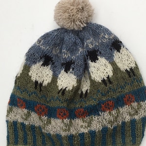 May include: A knitted wool hat with a pom-pom on top. The hat features a pattern of sheep and a blue, green, and orange stripe.