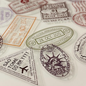 May include: A selection of transparent, vintage-style travel stamps featuring various designs and text. Stamps include phrases such as "U.S. Postage," "Malaysia Immigration," and "New York." The stamps are in shades of brown, green, and orange.
