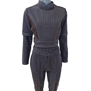 May include: A dark grey two-piece outfit with a high collar, long sleeves, and matching trousers. The top features vertical stitching and a waist belt. The trousers have pockets and brown patches. The outfit is displayed on a mannequin.