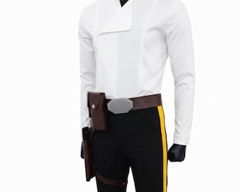 Pode incluir: Um conjunto de fantasia que inclui uma camisa branca de manga comprida com gola assimétrica e calças pretas com uma faixa amarela na lateral. O conjunto inclui um cinto castanho, uma coldre e uma fivela prateada.