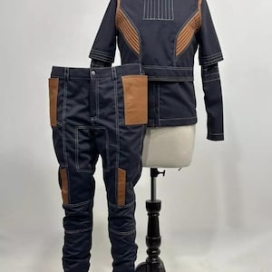 May include: A navy blue two-piece costume set, comprising a jacket and trousers. The jacket features brown shoulder and chest panels, with white stitching. The trousers have brown pockets and white stitching. The outfit is displayed on a mannequin.