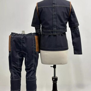 May include: A navy blue two-piece outfit with white stitching and brown leather accents. The jacket has a high collar and short sleeves. The pants have brown leather pockets. The outfit is displayed on a mannequin.