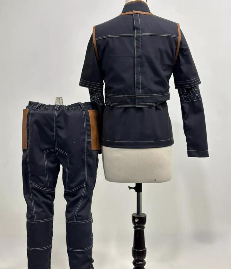 May include: A navy blue two-piece outfit with white stitching and brown leather accents. The jacket has a high collar and short sleeves. The pants have brown leather pockets. The outfit is displayed on a mannequin.