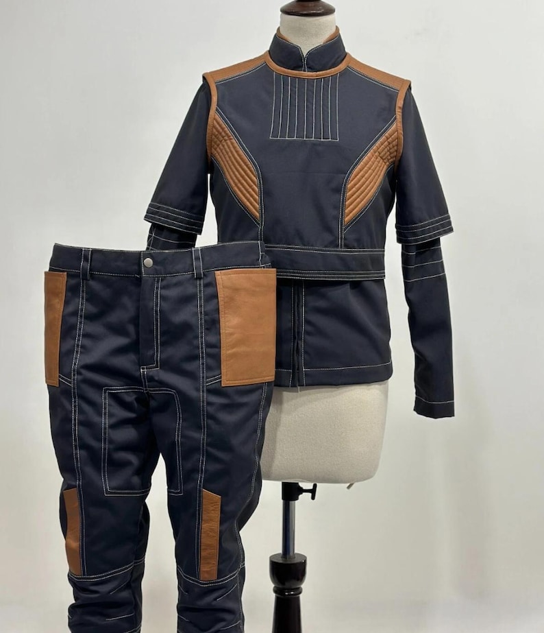 May include: A two-piece costume set featuring a navy blue jacket and pants. The jacket has brown accents and white stitching. The pants have brown pockets and white stitching. The costume is displayed on a mannequin.