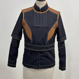 May include: A black jacket with brown accents and white stitching. The jacket features a stand-up collar, quilted panels, and a belt detail at the waist. The sleeves have a layered design.