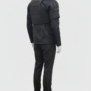 May include: Black tactical outfit, including a jacket with a vest, long-sleeve shirt, and cargo pants. The jacket has multiple pockets and reinforced panels. The pants have pockets on the sides. The outfit is displayed on a mannequin.