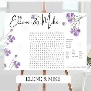 May include: A white wedding sign on an easel with the names "Ellene & Mike" in elegant script. The sign features a word search puzzle with wedding-related terms and floral accents in purple. The date "30 September 2026" is also displayed.