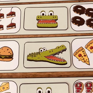 Puede incluir: Un conjunto de tarjetas ilustradas con imágenes de dibujos animados de alimentos y un cocodrilo verde con la boca abierta. Otras tarjetas muestran una hamburguesa, porciones de pizza y rosquillas.