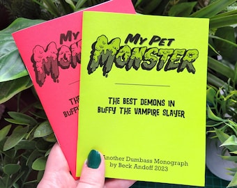 Op de afbeelding: Twee zines getiteld "My Pet Monster" worden getoond. Eén is felroze, de andere neon groen. De groene zine heeft de tekst "THE BEST DEMONS IN BUFFY THE VAMPIRE SLAYER" en "Another Dumbass Monograph by Beck Andoff 2023."