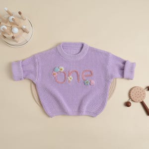 Custom First Birthday Sweater – Hand-Knit “One” Baby Girl Jumper – Personalized Lavender Outfit with Floral Appliques, Baby Gifts.