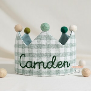 Può includere: Una corona per bambini con motivo a quadretti verdi e bianchi, con il nome "Camden" ricamato in verde. La corona è decorata con pompon colorati. Un accessorio affascinante per una festa di compleanno.
