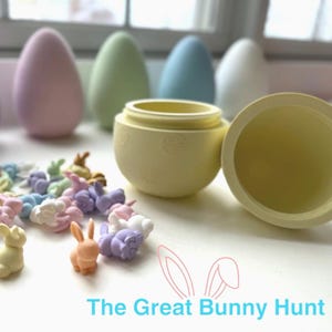May include: An open yellow egg-shaped container with a lid, surrounded by pastel-colored Easter eggs and small bunny figurines. The text "The Great Bunny Hunt" is displayed in blue.