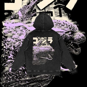 May include: Black hooded sweatshirt with a distressed look. The back of the sweatshirt features a graphic print of a Godzilla-like monster with the Japanese word "Gojira" printed above it.