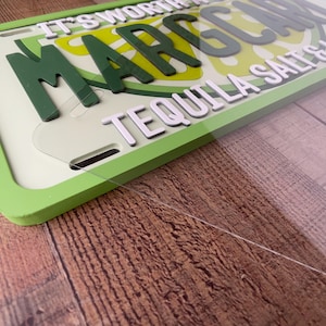 May include: A decorative license plate with the words "It's Worth the Margarita" in white and green lettering. The plate features a lime slice design and the phrase "Tequila Salts" in white. The plate has a green border.